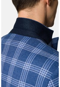 Niebieska marynarka w kratę z teksturowanej tkaniny, ciemną wełnianą kołnierzykiem i kontrastowym jaśniejszym niebieskim wzorem w kratę na korpusie.