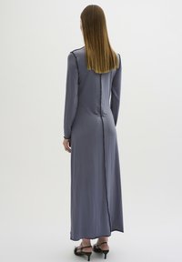 Langes, enganliegendes Kleid aus weichem grauem Stoff, mit langen Ärmeln, geradem Schnitt und einer kontrastierenden schwarzen Naht entlang des Rückens.