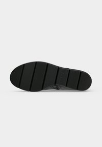 Semelle de chaussure noire avec des motifs de bande de roulement segmentés, des zones de grip texturées et le nom de la marque "Gabor" embossé près de la voûte plantaire.