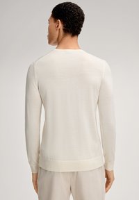 Maglione lavorato a maglia color crema chiaro con maniche lunghe, scollo rotondo e polsini e orlo a coste; texture liscia, design semplice senza motivi.