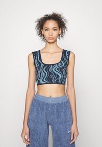 Top cropped em azul-marinho com um padrão turquesa ondulado. Apresenta um decote quadrado e alças largas. Combinado com calças largas de veludo cotelê azul.