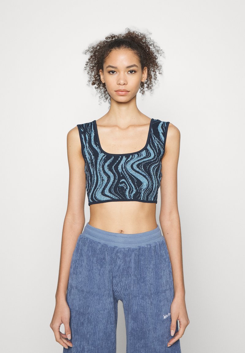 Top cropped em azul-marinho com um padrão turquesa ondulado. Apresenta um decote quadrado e alças largas. Combinado com calças largas de veludo cotelê azul.