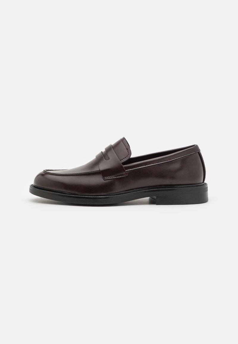 Mocassins en cuir marron avec une finition lisse, un bout arrondi, des détails de couture subtils et un talon en caoutchouc bas. Vue de côté affichée.