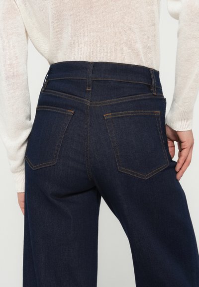 Tume sinised teksapüksid kõrge vöökohaga, oranži õmblusega ja kahe tagataskuga. Kangas on sileda, kergelt tekstuurse välimusega.