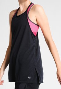 Svart atletisk linne med rosa detaljer. Har en lös passform, är ärmlöst, har sidslitsar och en logotyp i nedre vänstra hörnet.