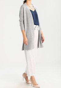 Ljusgrå lång cardigan med öppen frontdesign, mjukt textur, bärs över en marinblå topp och vita skräddarsydda byxor, kompletterad med ljusa skor.