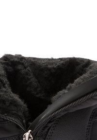 Prikaz izbliza crne zimske čizme s mekanim, pahuljastim crnim runom unutra i djelomično otvorenim srebrnim patentnim zatvaračem na teksturiranoj kožnoj vanjskoj površini.