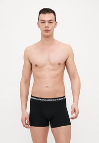 Boxer da uomo neri con design aderente, realizzati in tessuto morbido. Presentano una vita con logo a contrasto bianco e nero.