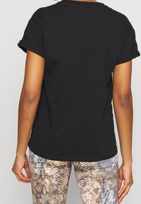 Camiseta negra de algodón con mangas cortas enrolladas y dobladillo redondeado. Combinada con leggings de estampado de serpiente en tonos neutros.
