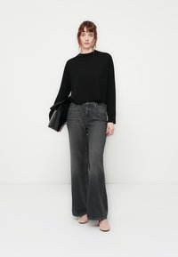Top nero a maniche lunghe abbinato a jeans grigi a vita alta e a gamba larga. La modella tiene una borsa nera e indossa delle ballerine color carne. Outfit semplice e casual.