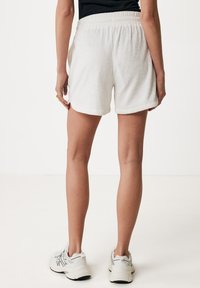 Shorts bianchi in spugna con vita elastica, caratterizzati da una vestibilità comoda e tasche laterali, abbinati a scarpe sportive grigio chiaro.