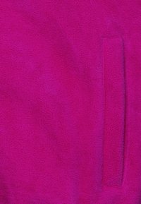 Tessuto in pile di un vivace fucsia, caratterizzato da una texture morbida. Una singola tasca a toppa è visibile sul lato destro.