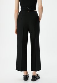 Zwarte wijde broek van een gladde stof, met een hoge taille en twee achterzakken. Draagt met zwarte schoenen voor een monochrome uitstraling.