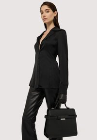 Černá saténová košile s knoflíky, v kombinaci s černými koženými kalhotami. Ve jedné ruce je držena strukturovaná černá kabelka s horním úchytem.