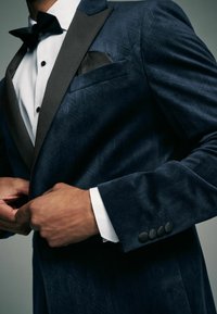 Marineblaues Samt-Tuxedo-Jackett mit geometrischem Muster, schwarzen Satin-Revers, einer Taschentuchtasche und schwarzen Knöpfen an den Ärmeln.