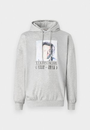 Ljusgrå hoodie med framfoto och texten "XXXTENTACION (1998 - 2018)" som hedrar den avlidna musikartisten.