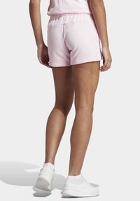 Ljusrosa bomullsshorts med resår i midjan, har en enkel design och är kombinerade med vita sportskor.