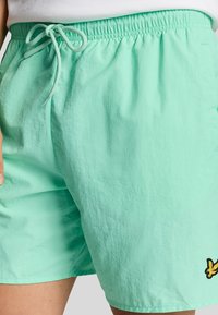 Costumini da bagno verde menta chiaro realizzati in un morbido tessuto testurizzato; presentano una vita elasticizzata con coulisse e un piccolo logo ricamato giallo.