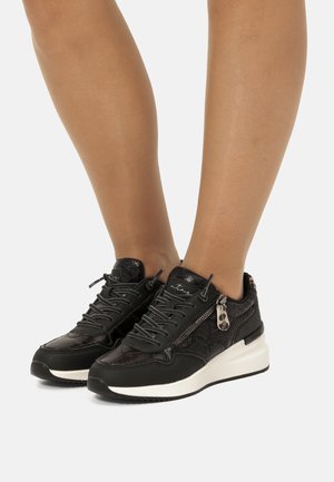 Baskets noires en cuir texturé, avec des détails zippés et une semelle blanche. Elles possèdent des lacets et un accent en métal décoratif au niveau du talon.