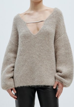 Light beige oversized sweater with a deep V-neck, ribbed texture, and wide sleeves. Features a silver hardware accent at the neckline.