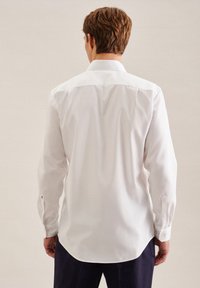 Hvit langermet skjorte med rett snitt, klassisk krage, knappedesign på ermene og en glatt tekstur, brukt sammen med mørke bukser.