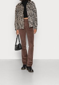 Veste en denim à motif léopard, crop top noir, pantalons évasés en velours côtelé marron, sac à main noir et bottes lacées noires.