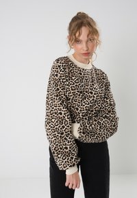 Sweatshirt en imprimé léopard avec des poignets et un col côtelés, offrant une coupe décontractée et une texture douce, associé à un jean noir.