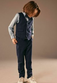 Námornícky oblek s vestou a nohavicemi, doplněný o světle modrou košili s vzorem a motýlkem. Bílé tenisky dokončují outfit.