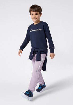 Sudadera azul marino con logo blanco de "Champion", pantalones deportivos morados claros con detalle de logo y zapatillas azul marino con acentos azules.
