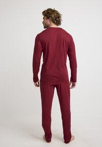 Red long-sleeve shirt and pants made of soft, lightweight fabric. Simple design with a relaxed fit, featuring a round neckline and long sleeves.