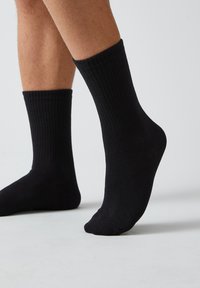 Calcetines negros acanalados de longitud media. Tejido suave y elástico con una textura lisa; sin patrones ni logotipos visibles.