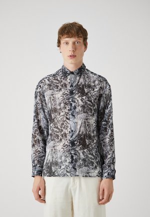Leichte, langärmlige Bluse mit einem schwarz-weißen abstrakten Muster, Knopfleiste und Kragen. Der Stoff wirkt glatt und glänzend.