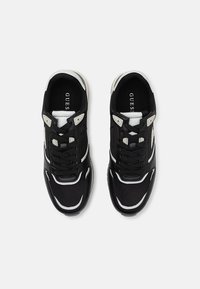 Zapatillas negras con una parte superior de cuero y malla, con detalles en blanco, una suela gruesa y un diseño tradicional de cordones. Logotipo en la lengüeta.