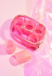 Contenedor transparente rosa con cremallera que contiene cuatro rulos de rizar en su interior, con una textura suave y detalle de superficie estriada. Acompañado de dos rulos adicionales.