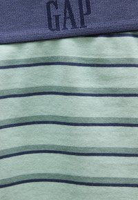 Tissu à rayures bleues et vertes avec logo "GAP" bleu marine brodé sur un col ou un poignet bleu uni.