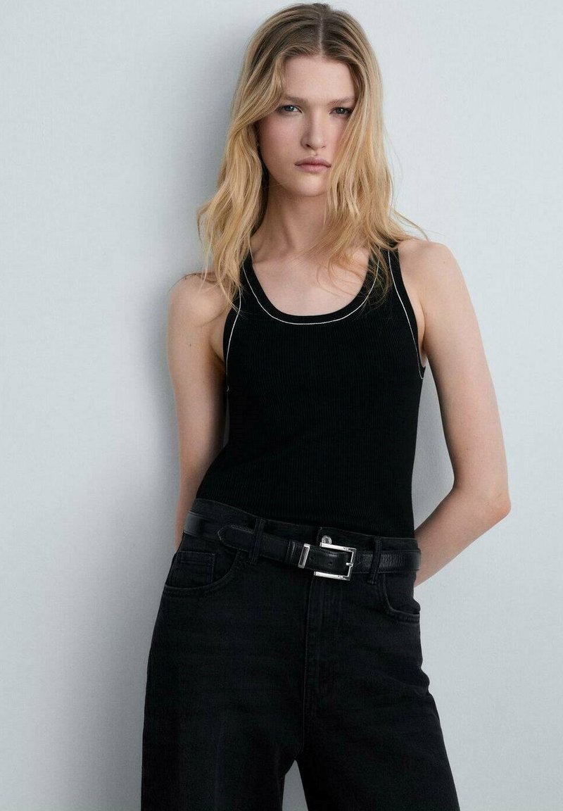 Top negru din material ribbed, cu o croială rotundă la gât și cusături albe decorative, purtat cu blugi negri denim cu talie înaltă și o curea neagră.
