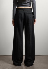 Pantaloni grigi scuri a gamba larga realizzati in tessuto morbido, con due tasche posteriori e una cintura liscia, caratterizzati da una silhouette rilassata e una caduta fluida.