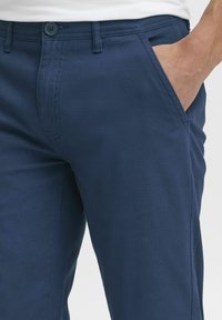 Pantalones de algodón azul marino con una textura suave, que cuentan con un bolsillo frontal y un cierre de botón. Corte ajustado con sutiles detalles de costura.