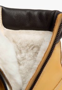 Braune Lederstiefel mit schwarzen Lederakzenten, ausgestattet mit einem weichen cremefarbenen Lammfellfutter und einem seitlichen Reißverschluss zum Schließen.