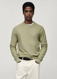 Hellgrüner Strickpullover mit strukturiertem Finish, Rundhalsausschnitt und gerippten Bündchen, kombiniert mit weißen Hosen und einem schwarzen Gürtel.