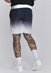 Férfi gradient sort, amely sötét tengernyitól fehérig terjed, fehér szegéllyel ellátott derékkal. Fehér sportcipők textúrázott talppal és bokazoknival.