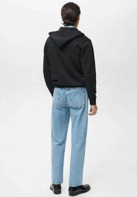 Sudadera negra con cordones, combinada con jeans rectos de color azul claro. Botines negros completan el atuendo. Diseño simple y casual.