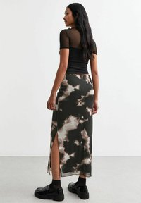 Top negro de malla de manga corta combinado con una falda larga y ajustada que presenta un patrón de nubes en negro y beige, y una abertura lateral. Calzado negro completa el look.