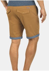 Pantaloni corti marroni in cotone, con risvolto in denim, due tasche posteriori con chiusura a bottone e un'etichetta sulla vita.