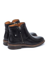 Bottines noires en cuir avec une fermeture éclair latérale et une semelle marron, présentant une texture lisse et des lignes épurées. Intérieur accentué de l'orange.