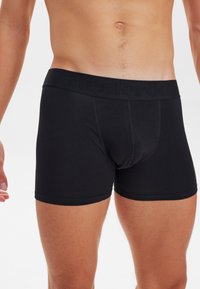 Boxer ajustados negros con una cinturilla suave y elástica con marca grabada. El material es liso, tiene un diseño ceñido y no presenta patrones visibles.