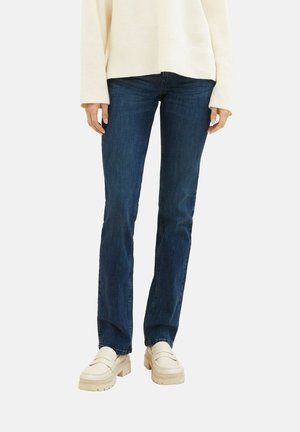 Slim-fit mørkeblå jeans båret med en cremefarvet sweater og beige chunky loafers, vist på en stående person fra talje til fødder.