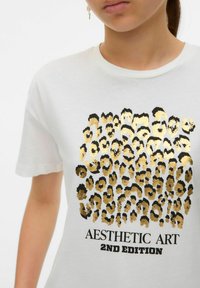T-shirt en coton blanc avec un motif léopard noir et or, portant le texte "AESTHETIC ART 2ND EDITION" en bas. Manches courtes.