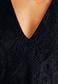 Μαύρο λευκό ύφασμα με περίπλοκα λουλούδια, με σχέδιο βαθού του V και υφή επιφάνειας.