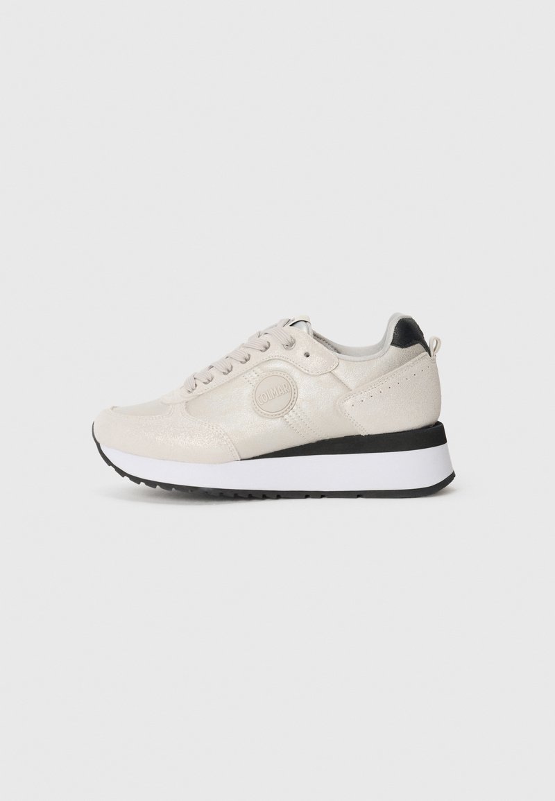 Sneakers bege claro com acabamento brilhante, bico redondo, atilhos na frente, detalhe preto no calcanhar e sola de borracha branca com tração.